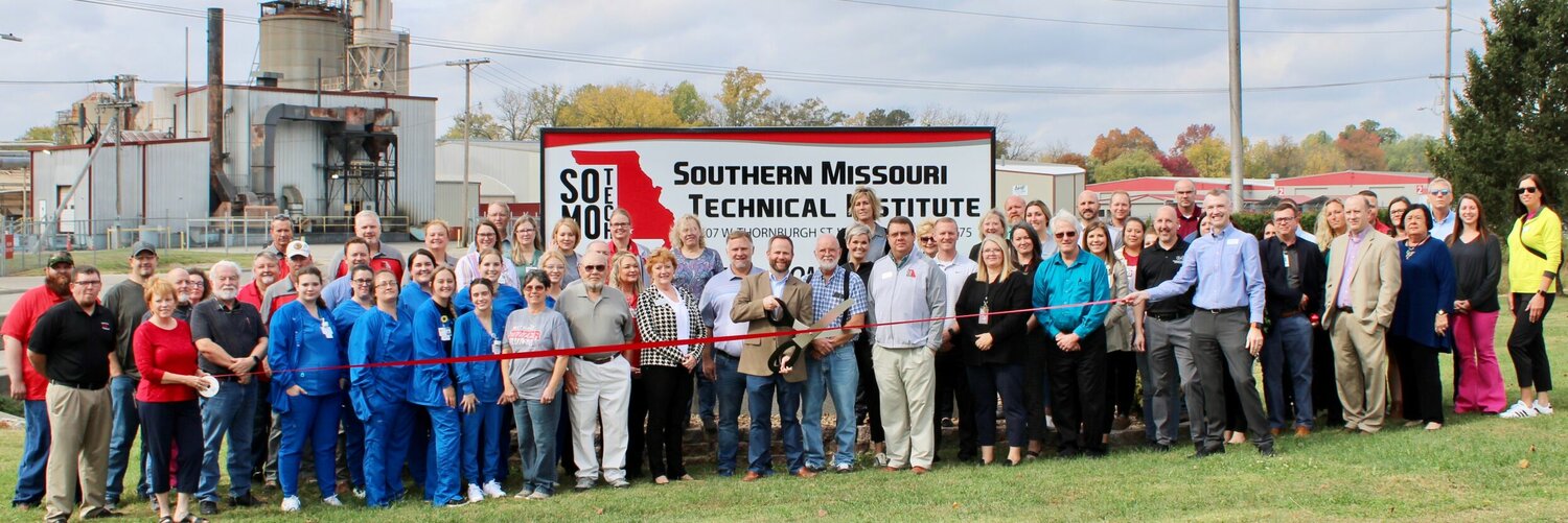 More than five dozen students, current and past faculty, representatives of West Plains R-7 School District administration and members of the Greater West Plains Area Chamber of Commerce gathered Oct. 25 to christen the recently renamed Southern Missouri Technical Institute (SoMoTech), formerly the South Central Career Center. Norris Cozort was in attendance as an instructor that taught at the vocational school at its beginning. The facility is operated by the West Plains R-7 district, and accepts high school and adult students in training programs in agriculture, auto body and collision repair, auto mechanics technology, carpentry, commercial and advertising art, culinary arts, drafting technology, family and consumer science, and health sciences including practical nursing, surgical technology and welding. It is accredited by the Commission of the Council on Occupational Education and the Missouri Department of Elementary and Secondary Education (DESE) and several program-specific accrediting agencies. Cutting the ribbon is SoMoTech Director Dr. Josh Cotter, who spearheaded the process to change the name. With him, to his right, are School Board President Jim Thompson and Superintendent Dr. Wes Davis.